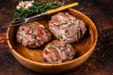 Ahşap bir tabakta kuzu budu bifteği ve otlar. Karanlık arka plan. Üst görünüm