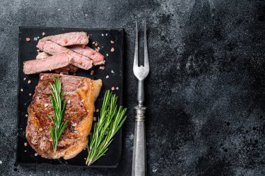 Kavrulmuş New York bifteği ya da mermer bir tahtanın üzerinde striploin. Siyah arka plan. Üst Manzara. Boşluğu kopyala