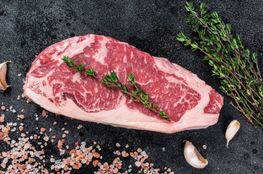 Kasap masasında tuzlu ve kekikli çiğ biftek. Siyah arka plan. Üst görünüm