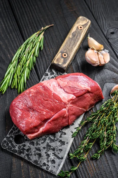 Raw lamb meat fillet steak on a cleaver. Black wooden background. Top view