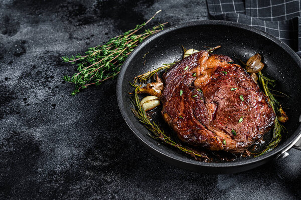 Roasted rib eye steak, ribeye beef meat in a pan. Black background. Top view. Copy space