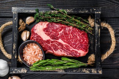 Ham pirzola bifteği kasap ahşap tepside otlarla birlikte. Siyah ahşap arka plan. Üst görünüm