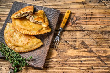 Tahta kesme tahtasının üzerinde servis edilen kıymalı et ile dolu Şili usulü kızarmış börekler. Ahşap arka plan. Üst Manzara. Boşluğu kopyala