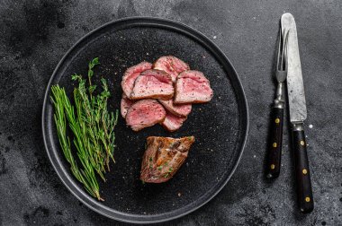 Barbekü ızgara ve dilimlenmiş dana fileto bifteği tabakta. Siyah arka plan. Üst görünüm