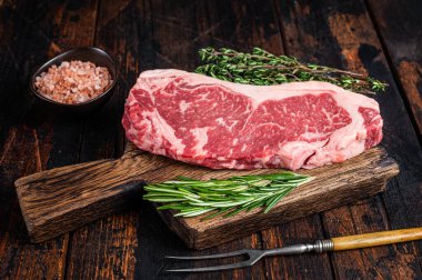Çiğ New York bifteği ya da tahta bir tahtanın üzerinde striploin. Koyu ahşap arka plan. Üst görünüm