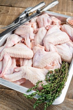 Mutfak tepsisinde taze çiğ tavuk kanadı ve bitkilerle birlikte tavuk eti. Ahşap arka plan. Üst görünüm