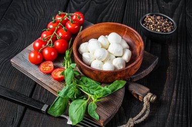İtalyan küçük Mozzarella peynir topları, fesleğen ve domates kirazı Caprese salatası pişirmeye hazır. Siyah ahşap arka plan. Üst görünüm
