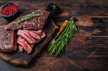 Kesme tahtasının üzerinde otlarla birlikte ızgara et bifteği. Koyu ahşap arka plan. Üst Manzara. Boşluğu kopyala