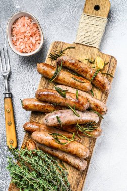 Kesme tahtasında ızgara sosis ve şifalı bitkiler. Beyaz arka plan. Üst görünüm