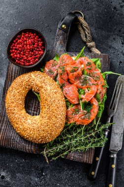 Yumuşak peynirli füme somon simidi, ahşap kesim tahtasında roka. Siyah arka plan. Üst görünüm