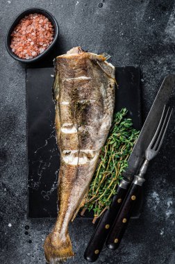 Misket tahtasında kekik olan kızarmış morina balığı. Siyah arka plan. Üst görünüm