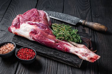 Pişmemiş kuzu budu ve kasap kesme tahtasında otlar. Siyah ahşap arka plan. Üst görünüm