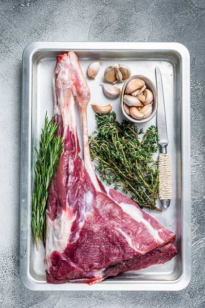 Uncooked Raw goat or lamb leg with herbs in baking tray. White background. Top view — Stock Photo, Image
