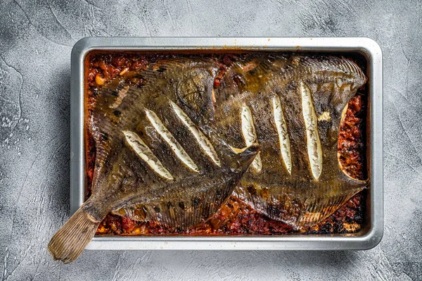 Flounder flat fish roasted in a tomato sauce in baking tray. White background. Top view