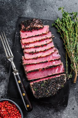 Az pişmiş ton balıklı biftek dilimleri ve kesme tahtasında taze otlar. Siyah arka plan. Üst görünüm