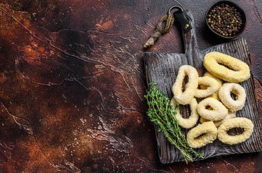 Kesme tahtasındaki ekmek kırıntılarında donmuş çiğ mürekkep balığı halkaları. Karanlık arka plan. Üst Manzara. Boşluğu kopyala