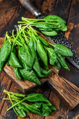 Tahta kesme tahtasının üzerinde küçük ıspanak yaprakları. Koyu ahşap arka plan. Üst görünüm