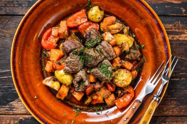 Tabakta sebzeyle pişirilmiş sığır eti. Koyu ahşap arka plan. Üst görünüm