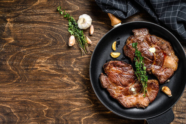 Grilled marble meat steaks Chuck eye roll in a pan. Dark wooden background. Top view. Copy space