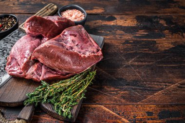 Çiğ sığır eti ya da et satırıyla kesilmiş bir tahta üzerinde dana kalbi. Koyu ahşap arka plan. Üst Manzara. Boşluğu kopyala