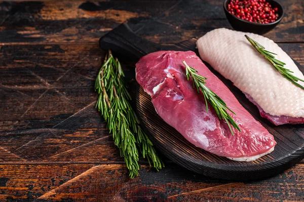 Bifes de filé de peito de pato cru em placa de corte de madeira com alecrim. Fundo de madeira escuro. Vista superior. Espaço de cópia — Fotografia de Stock