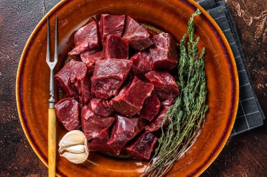 Sığır eti ya da çiğ kalbi kırsal bir tabakta otlarla kes. Karanlık arka plan. Üst Görünüm