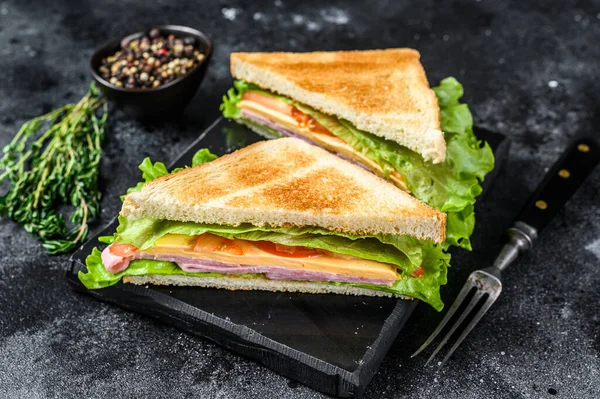 Club-Sandwiches mit Schweineschinken, Käse, Tomaten und Salat auf einem Holzschneidebrett. Schwarzer Hintergrund. Ansicht von oben — Stockfoto