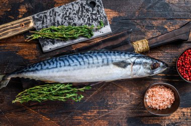 Taze çiğ balık uskumrusu bir satırla tahta bir kesme tahtasının üzerinde. Koyu ahşap arka plan. Üst görünüm