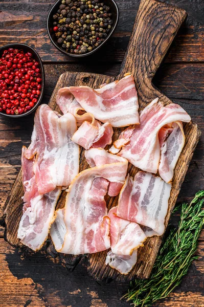 Raw pork bacon meat slices on a wooden cutting board. Dark wooden background. Top view — Stock Photo, Image