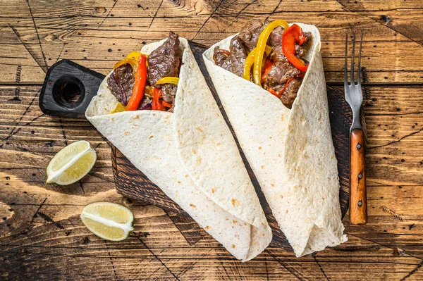 Fajitas Envoltura de tortilla con rayas de carne de res, pimiento morrón de colores y cebolla y salsa. Fondo de madera. Vista superior —  Fotos de Stock