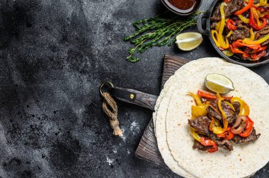 Biftek Fajitas, tortilla, biber ve soğan karışımı geleneksel Meksika yemekleri. Siyah arka plan. Üst Manzara. Boşluğu kopyala