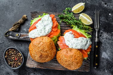 Tuzlu somonlu balık burger, avokado, hardal sosu, salatalık ve buzdağı salatası. Siyah arka plan. en üstteki görünüm