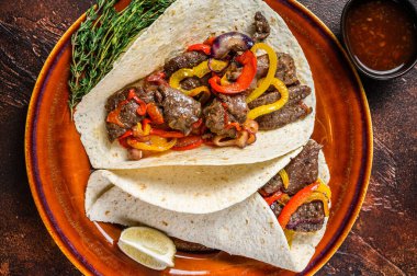 Fajitas Tortilla biftek şeritleri, tatlı biber ve soğanla sarılır. Karanlık ahşap arka plan. Üst görünüm