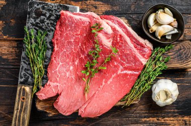 Kesme tahtasının üzerinde çiğ et, pirzola ve biftek. Koyu ahşap arka plan. Üst görünüm