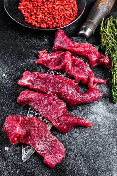 Raw marbled meat cut into thin strips for beefstroganoff. Black background. Top view