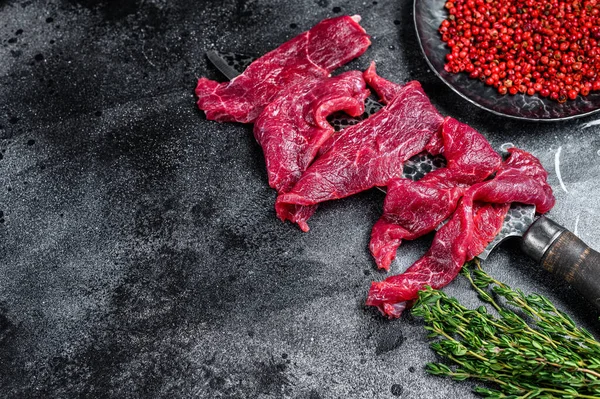 Obehandlat marmorerat kött som styckats i tunna strimlor för biff. Svart bakgrund. Högst upp. Kopiera utrymme — Stockfoto