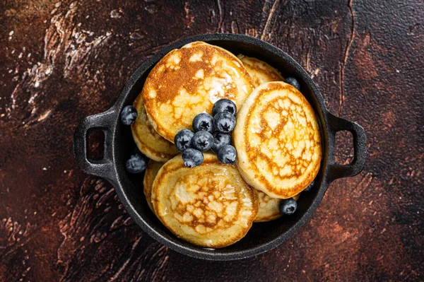 Gebratene Pfannkuchen mit frischen Blaubeeren und Ahornsirup in einer Pfanne. Dunkler Hintergrund. Ansicht von oben — Stockfoto