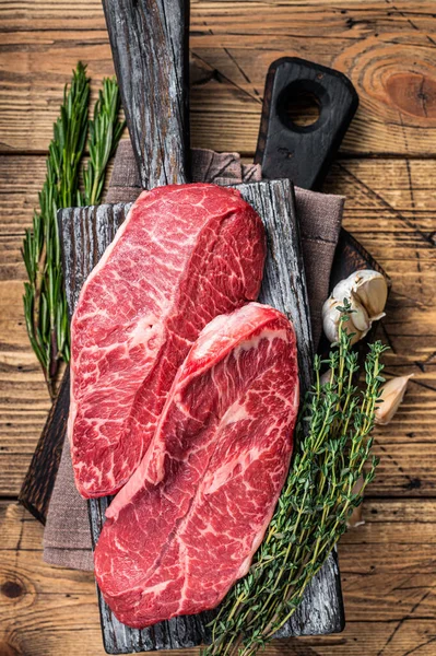 Tahta bir kasap tahtasında çiğ omuz üstü bıçaklı biftek ve otlar. Ahşap arka plan. Üst Görünüm — Stok fotoğraf