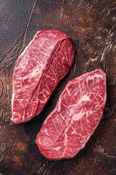Raw Top Blade or flat iron beef meat steaks on a butcher table. Dark background. Top View