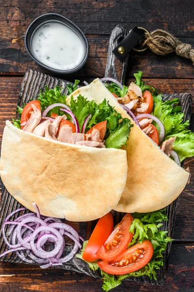Greckie gyros zawinięte w pieczywo pita z warzywami i sosem. Ciemne drewniane tło. Widok z góry — Zdjęcie stockowe