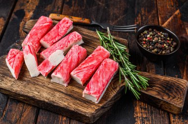 Tahta kesme tahtasına dilimlenmiş yengeç surimi çubukları. Koyu ahşap arka plan. Üst görünüm