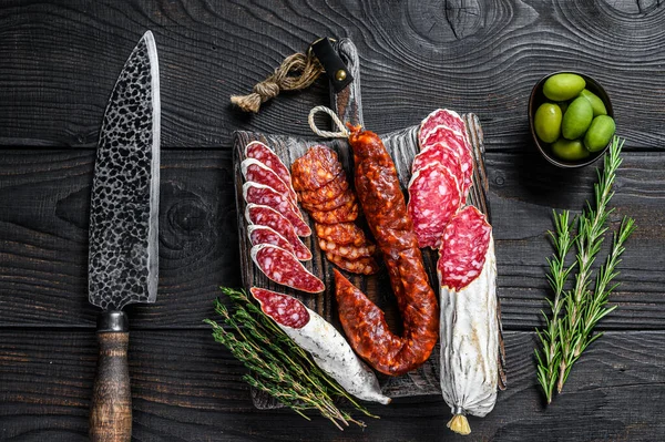 Espanhol tapas salsichas fatiadas salame, fuet e chouriço em uma tábua de corte de madeira. Fundo de madeira preta. Vista superior — Fotografia de Stock