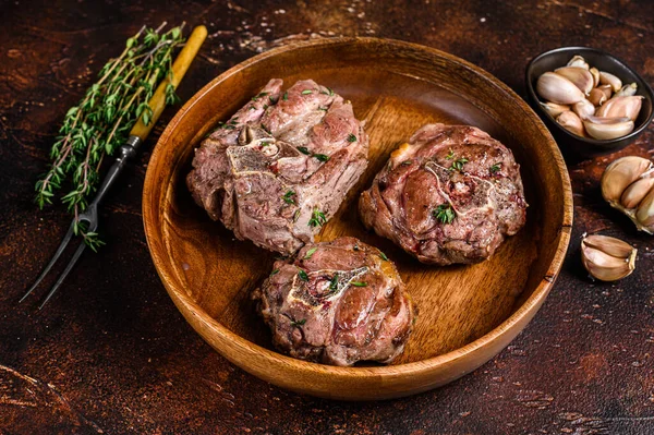 Ahşap bir tabakta kuzu budu bifteği ve otlar. Karanlık arka plan. Üst görünüm