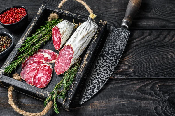 Slices of dry cured salchichon salami in a wooden tray. Black wooden background. Top view. Copy space — Stock Photo, Image