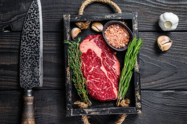 Ham pirzola bifteği kasap ahşap tepside otlarla birlikte. Siyah ahşap arka plan. Üst görünüm