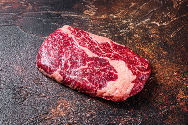 Raw rib eye beef meat steak on a butcher table prepared for the cooking. Dark background. Top view