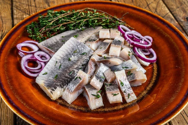 Filete cortado en rodajas de pescado de arenque marinado en escabeche en un plato con tomillo y cebolla. fondo de madera. Vista superior — Foto de Stock