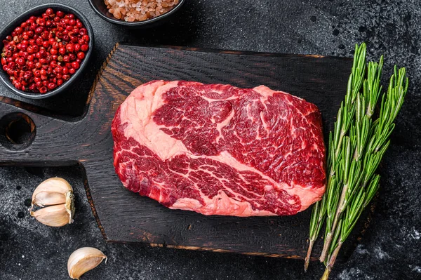 Černý angus ribeye, syrový steak z hovězího žebra na dřevěné desce s nožem. Černé pozadí. Horní pohled — Stock fotografie