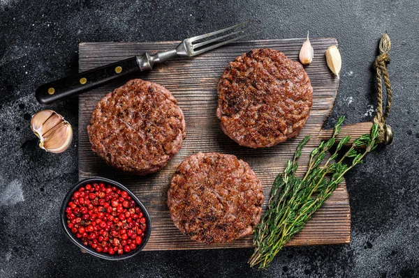 Churrasco grelhado carne de vaca rissóis para hambúrguer de carne picada e ervas em uma placa de madeira. Fundo preto. Vista superior — Fotografia de Stock