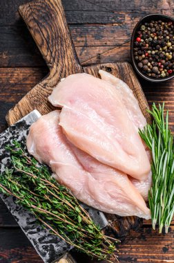 Çiğ kesilmiş tavuk göğsü fileto pirzolaları tahta bir kesme tahtasının üzerinde satırla. Koyu ahşap arka plan. Üst görünüm